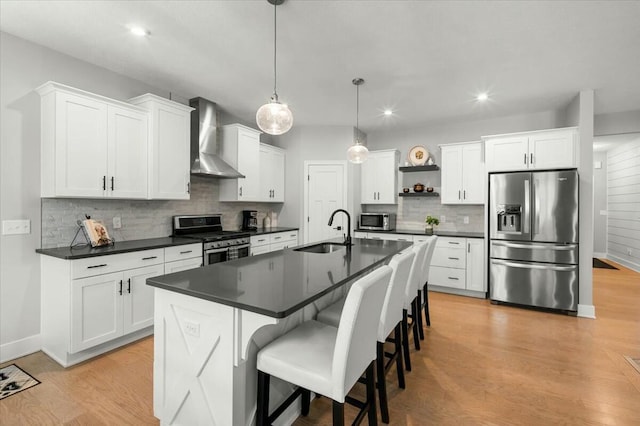 kitchen featuring light wood-style flooring, a sink, appliances with stainless steel finishes, wall chimney exhaust hood, and dark countertops