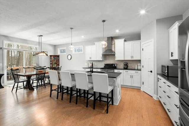 kitchen featuring dark countertops, light wood-style floors, wall chimney exhaust hood, and appliances with stainless steel finishes