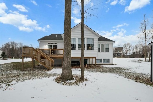 snow covered back of property with stairs and a wooden deck