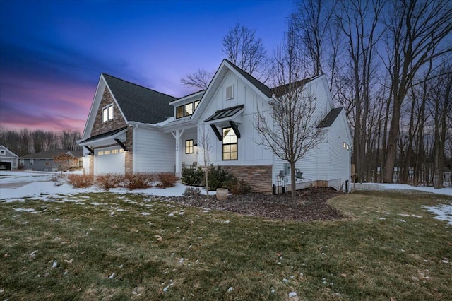 snow covered property featuring a garage, stone siding, board and batten siding, and a yard