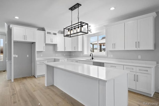 kitchen featuring a kitchen island, pendant lighting, white cabinetry, sink, and light hardwood / wood-style flooring