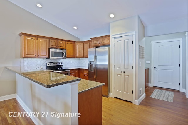 100 Tuscany Cir, Saginaw, MI 48603 - kitchen featuring stainless steel appliances, a peninsula, brown cabinetry, stone countertops, and lofted ceiling