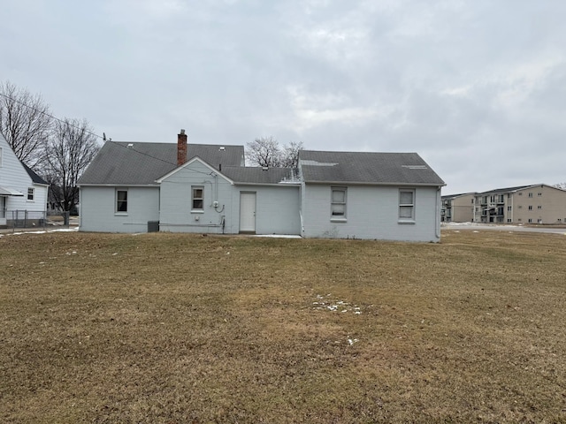 rear view of house with a shingled roof, a lawn, and a chimney