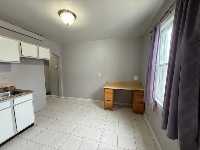 kitchen featuring arched walkways, white cabinets, a sink, and baseboards