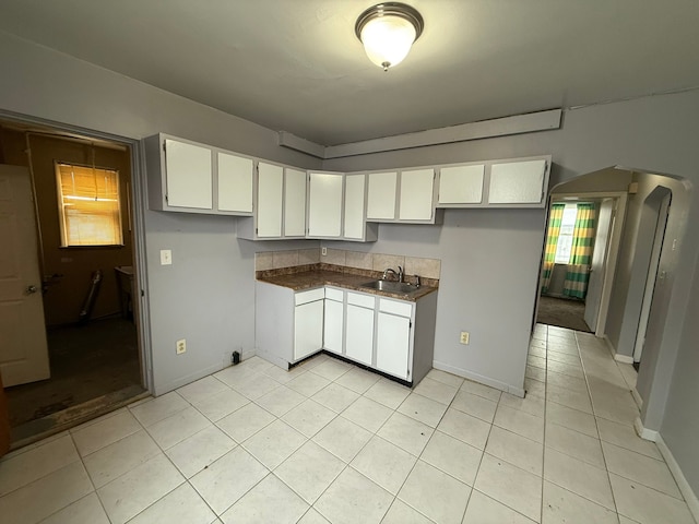 kitchen featuring dark countertops, white cabinetry, a sink, and arched walkways