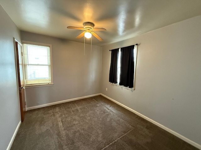 spare room with dark colored carpet, a ceiling fan, and baseboards