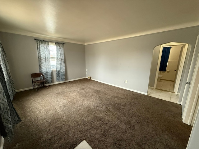 spare room featuring arched walkways, light tile patterned floors, baseboards, and light colored carpet