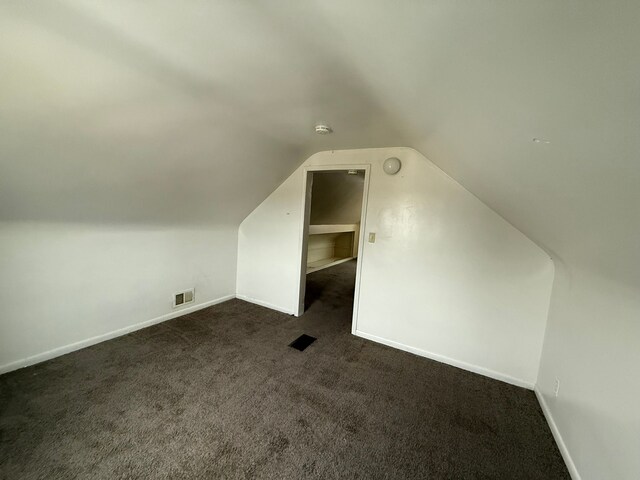 additional living space with baseboards, visible vents, vaulted ceiling, and dark colored carpet