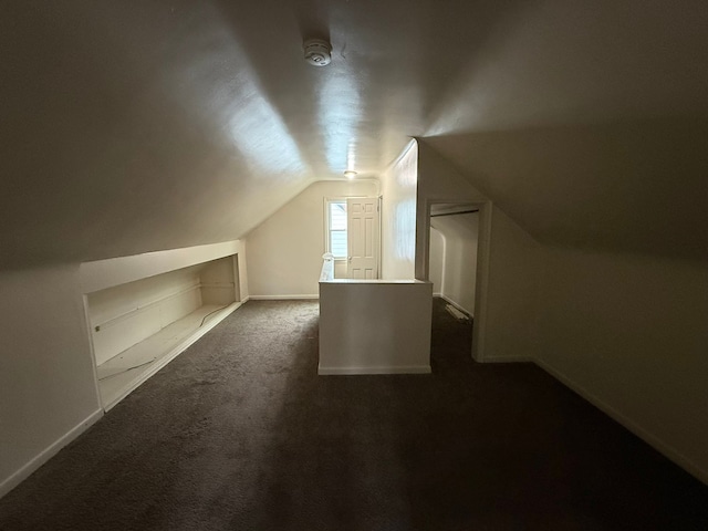 additional living space featuring vaulted ceiling, baseboards, and dark colored carpet