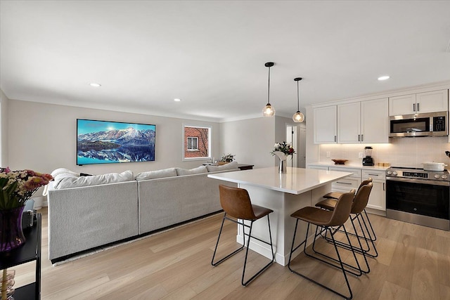 kitchen featuring appliances with stainless steel finishes, a kitchen bar, white cabinetry, hanging light fixtures, and an island with sink