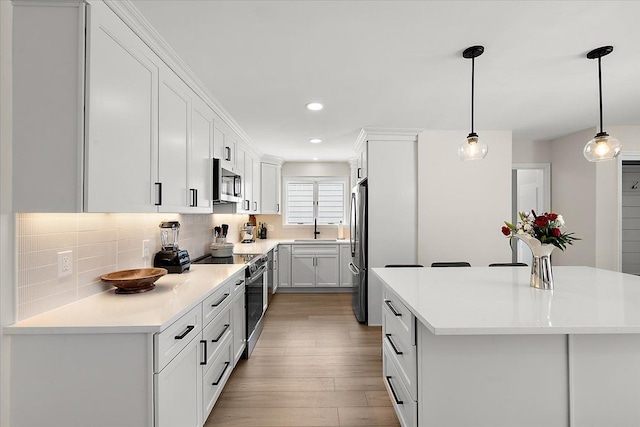 kitchen featuring white cabinetry, a kitchen island, hanging light fixtures, and stainless steel appliances