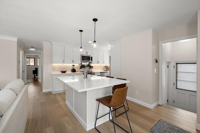 kitchen with stainless steel appliances, light hardwood / wood-style flooring, white cabinets, a kitchen bar, and pendant lighting