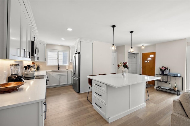 kitchen featuring appliances with stainless steel finishes, sink, a center island, decorative light fixtures, and white cabinets