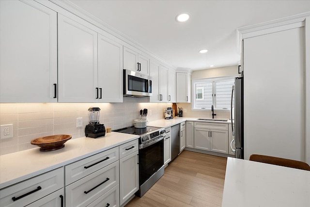 kitchen with appliances with stainless steel finishes, sink, light hardwood / wood-style flooring, white cabinets, and decorative backsplash