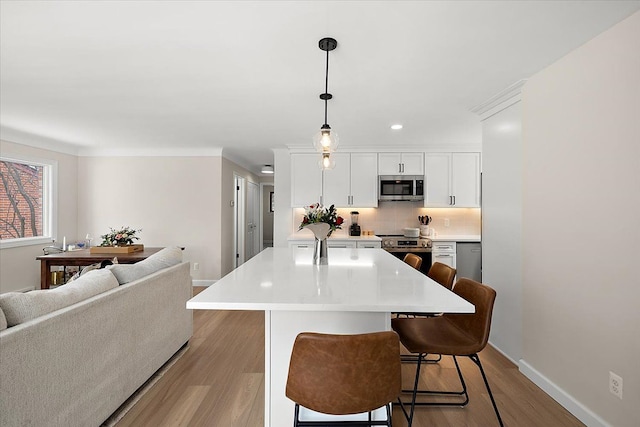 kitchen with stainless steel appliances, light hardwood / wood-style floors, pendant lighting, a breakfast bar, and white cabinetry