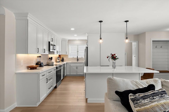 kitchen with light hardwood / wood-style flooring, pendant lighting, a kitchen island, stainless steel appliances, and white cabinets