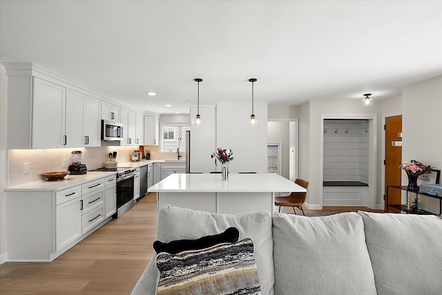 kitchen with hanging light fixtures, stainless steel appliances, light hardwood / wood-style flooring, white cabinets, and decorative backsplash