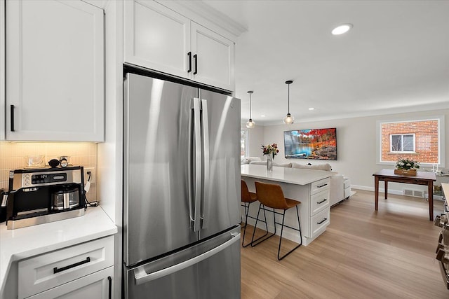 kitchen featuring white cabinetry, kitchen peninsula, stainless steel refrigerator, backsplash, and pendant lighting