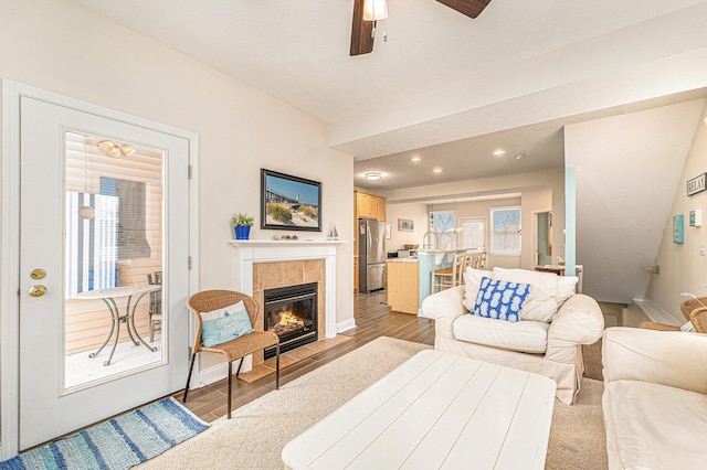 living room with a tiled fireplace, ceiling fan, a healthy amount of sunlight, and light hardwood / wood-style floors