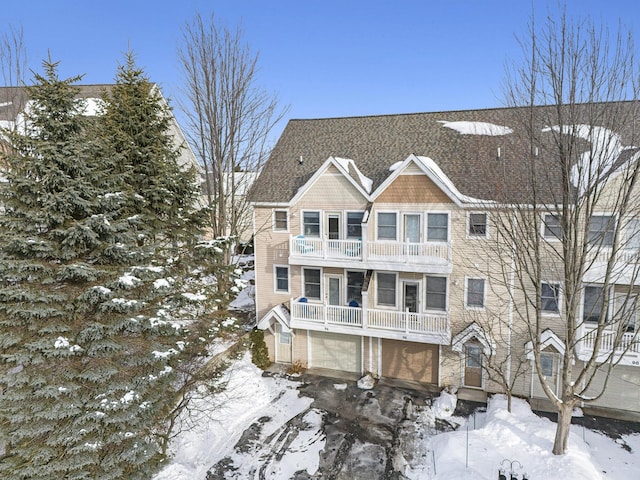 snow covered rear of property featuring a balcony and a garage