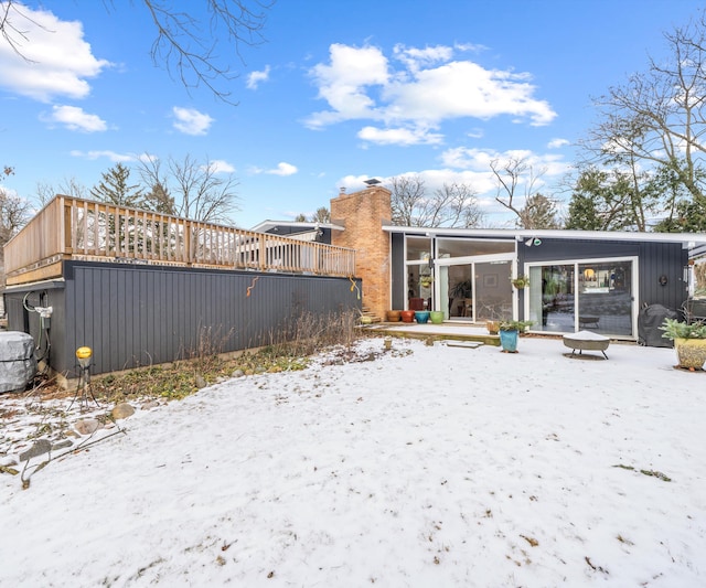 snow covered back of property with a wooden deck