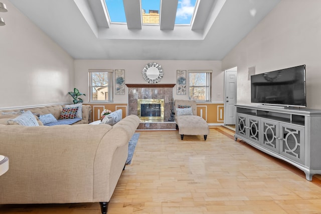 living area with lofted ceiling with skylight, light wood-style floors, a raised ceiling, and a fireplace