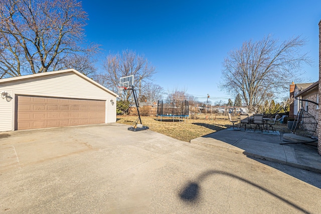 view of yard with a trampoline, fence, a garage, an outdoor structure, and a patio