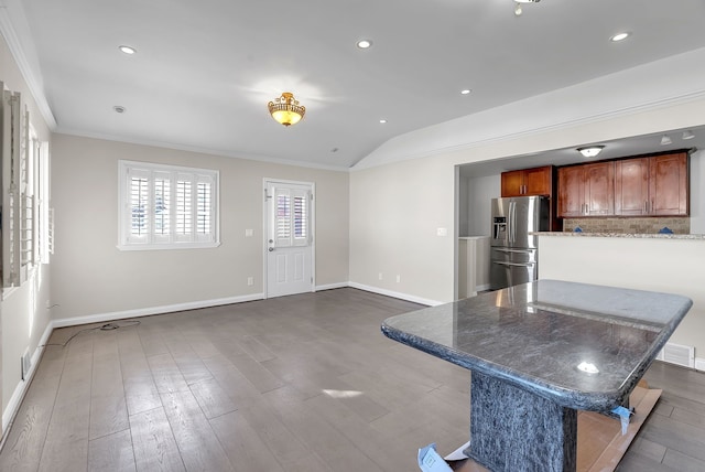 kitchen with dark wood-style floors, ornamental molding, vaulted ceiling, stainless steel fridge, and a kitchen bar