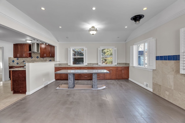 kitchen with a peninsula, wall chimney exhaust hood, vaulted ceiling, and wood finished floors