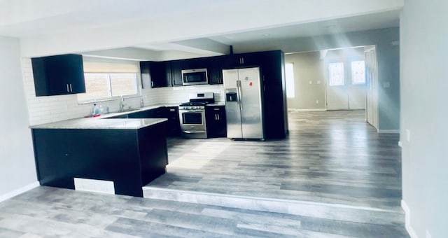 kitchen with sink, decorative backsplash, light hardwood / wood-style floors, kitchen peninsula, and stainless steel appliances