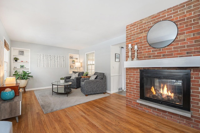 unfurnished living room featuring built in shelves, wood-type flooring, and a fireplace