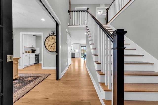 entryway with light wood finished floors, baseboards, a towering ceiling, wine cooler, and stairs