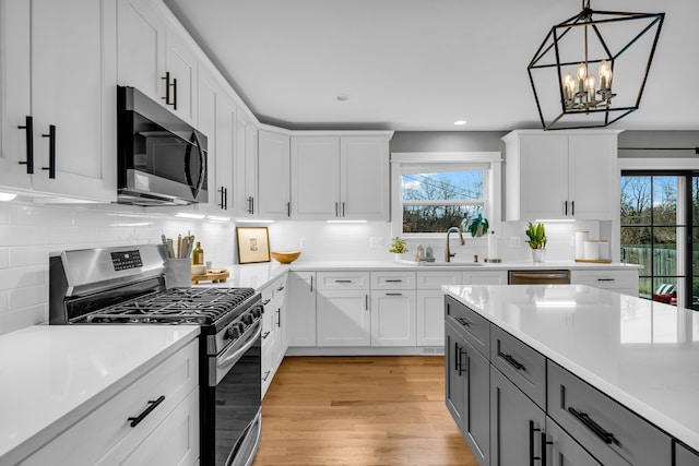 kitchen with white cabinets, appliances with stainless steel finishes, hanging light fixtures, light countertops, and gray cabinetry