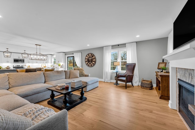 living area with a notable chandelier, a fireplace, recessed lighting, light wood-type flooring, and baseboards