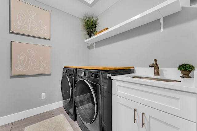 laundry room with cabinet space, baseboards, light wood-style flooring, washing machine and dryer, and a sink