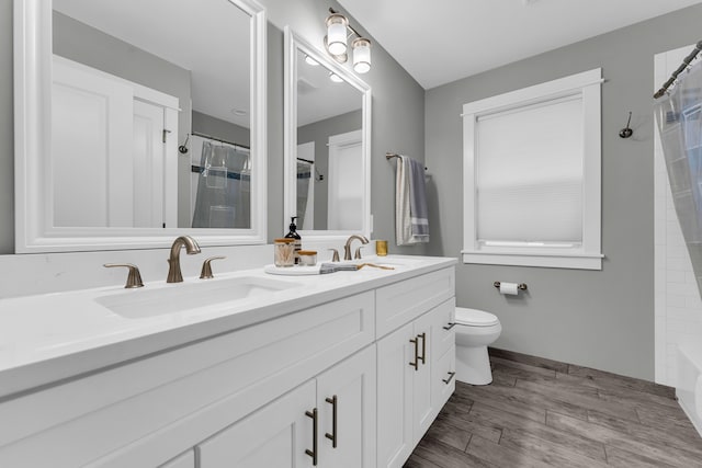 bathroom with double vanity, toilet, a sink, and wood finished floors