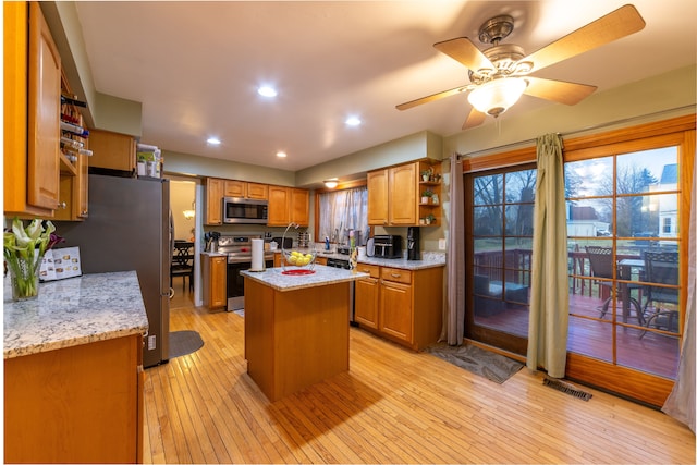 kitchen with ceiling fan, appliances with stainless steel finishes, a center island, light hardwood / wood-style floors, and light stone countertops