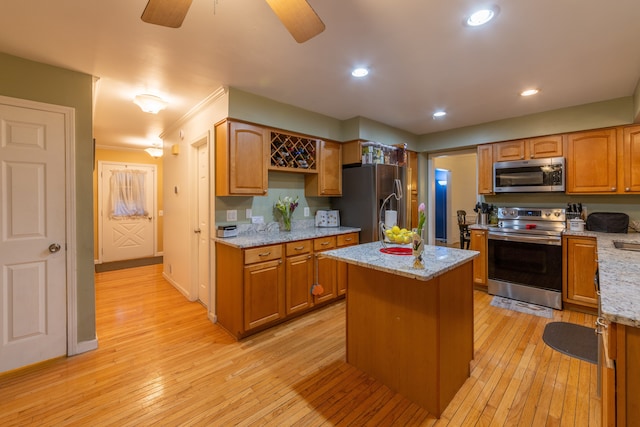 kitchen featuring a center island, ceiling fan, light stone counters, stainless steel appliances, and light wood-type flooring