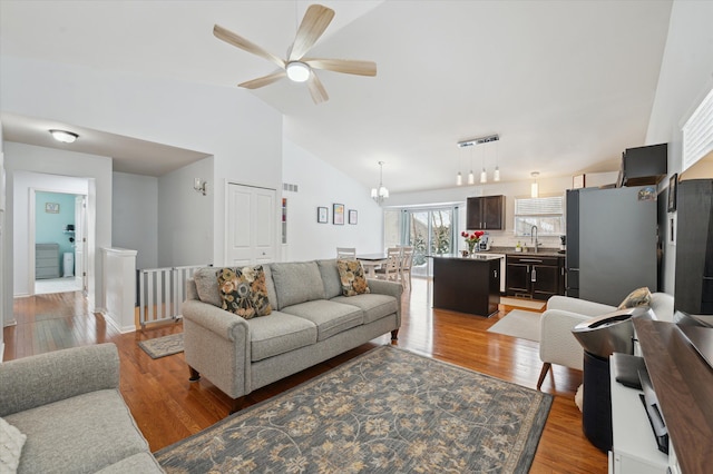 living room with high vaulted ceiling, sink, ceiling fan with notable chandelier, and light wood-type flooring