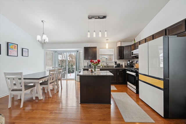 kitchen with lofted ceiling, a center island, stainless steel range with gas stovetop, white fridge, and pendant lighting