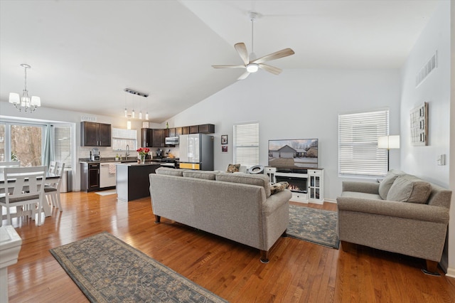 living room featuring ceiling fan with notable chandelier, high vaulted ceiling, sink, and light hardwood / wood-style floors