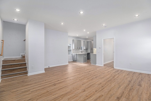 unfurnished living room with light wood-style flooring, stairs, recessed lighting, and baseboards