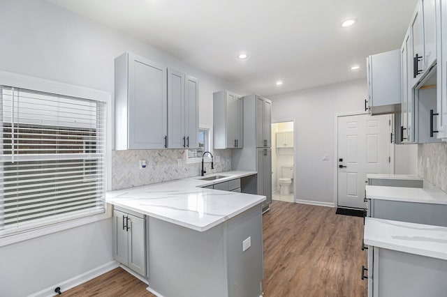 kitchen with wood finished floors, a sink, decorative backsplash, a peninsula, and gray cabinetry