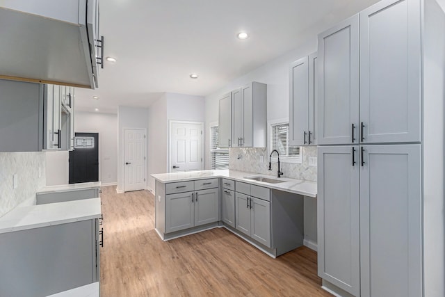 kitchen with light wood-style floors, gray cabinetry, a sink, and tasteful backsplash