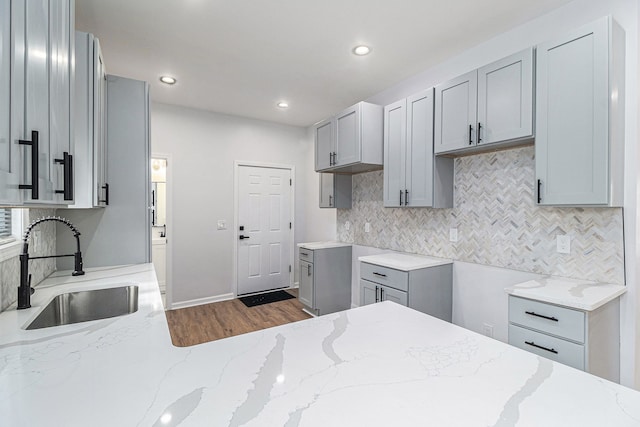 kitchen featuring light stone counters, gray cabinetry, a sink, and tasteful backsplash