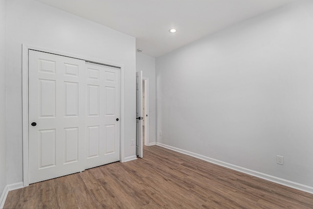 unfurnished bedroom with baseboards, a closet, recessed lighting, and wood finished floors