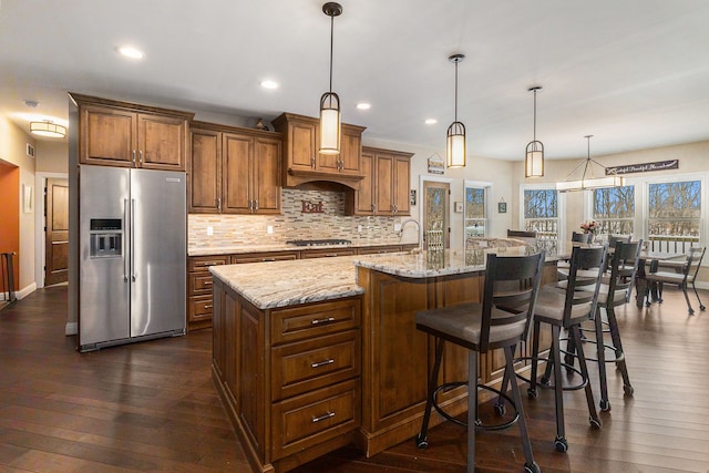 kitchen with brown cabinets, pendant lighting, a large island, stainless steel appliances, and dark wood-style flooring