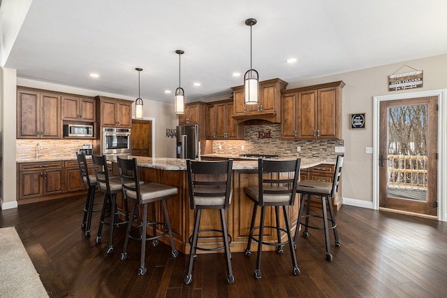 kitchen with hanging light fixtures, light stone counters, a large island, stainless steel appliances, and brown cabinetry