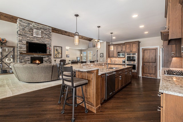 kitchen with appliances with stainless steel finishes, open floor plan, a sink, decorative light fixtures, and a spacious island