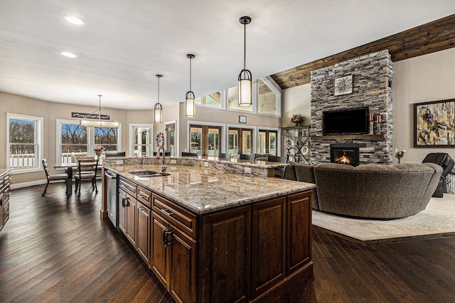 kitchen featuring hanging light fixtures, light stone counters, a sink, a kitchen island with sink, and dark brown cabinetry